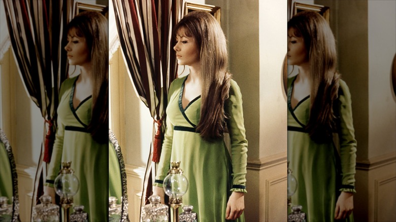 Ingrid Pitt regarde par la fenêtre avec des cheveux longs et une robe verte