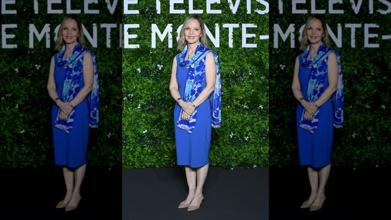 Melissa Sue Anderson sourit en portant une robe midi bleu colbalt et une écharpe bleu colbalt et bleu clair