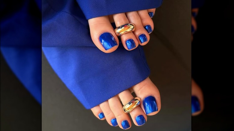 Une pédicure avec du vernis à ongles bleu chrome et des bagues d'orteil dorées