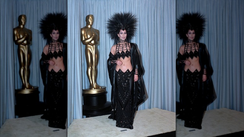 Cher porte un ensemble deux pièces noir scintillant et une coiffe à plumes aux Oscars de 1986