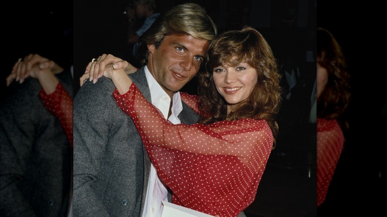 Victoria Principal portant un haut transparent à pois rouges et blancs serrant Christopher Skinner dans ses bras vers 1979.