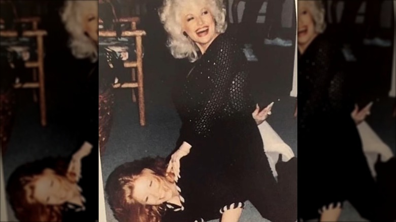 Judy Ogle est allongée sous Dolly Parton, vêtue d'un ensemble noir et ses cheveux roux étalés sur le sol