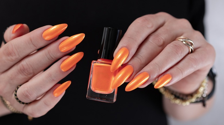 Mains avec manucure orange vif tenant une bouteille de vernis à ongles orange