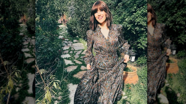Erin Krakow est vue tenant la jupe d'une robe fluide à motifs devant un fond de verdure pittoresque