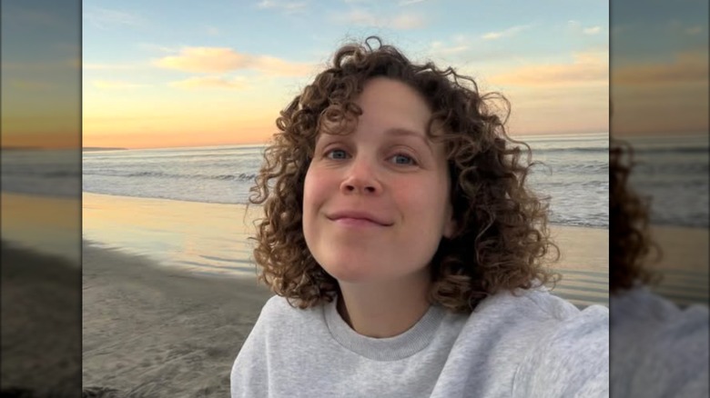 Erin Krakow pose pour un selfie au lever du soleil sur la plage tout en portant un sweat-shirt gris et ses boucles naturelles
