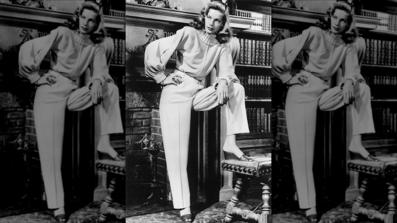 Lauren Bacall pose près d'une cheminée dans un pull à col roulé Leah Rhodes, un pantalon décontracté et des mules compensées en décembre 1946