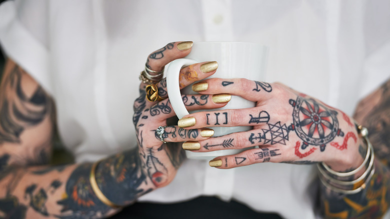 Une personne avec des mains et des jointures tatouées tenant une tasse