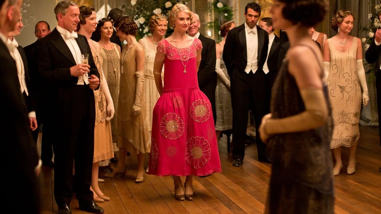 Lily James dans le rôle de Lady Rose portant une robe rose vif à taille basse avec des ornements floraux