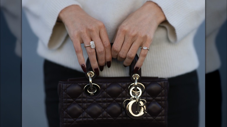 Une femme aux ongles rouge vin foncé tenant un sac à main.