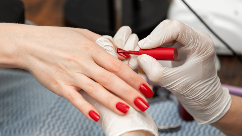 Une femme qui se fait peindre les ongles en rouge.