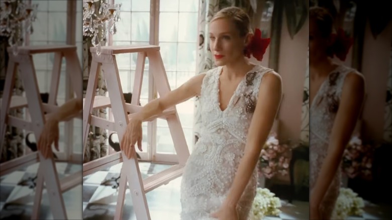 Sarah Jessica Parker dans le rôle de Carrie Bradshaw portant une robe de mariée en dentelle à queue de poisson avec une fleur rouge dans les cheveux.