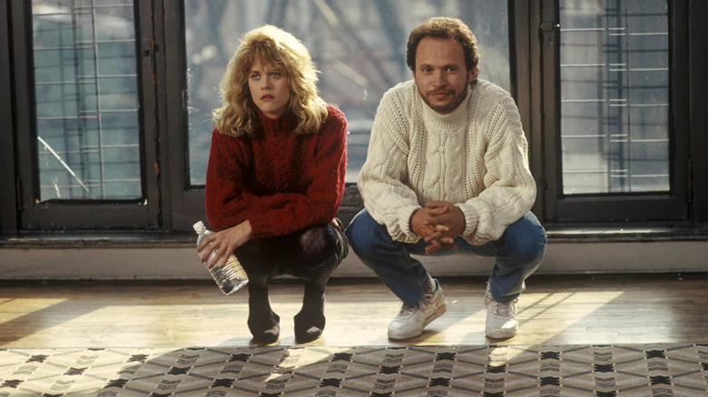Meg Ryan portant un pull en tricot rouge accroupie à côté de Billy Crystal portant un pull en tricot blanc 